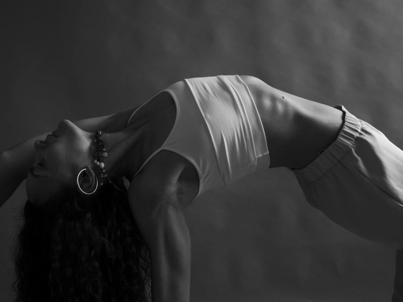 A person in a calm, focused yoga pose against a minimalist dark backdrop.